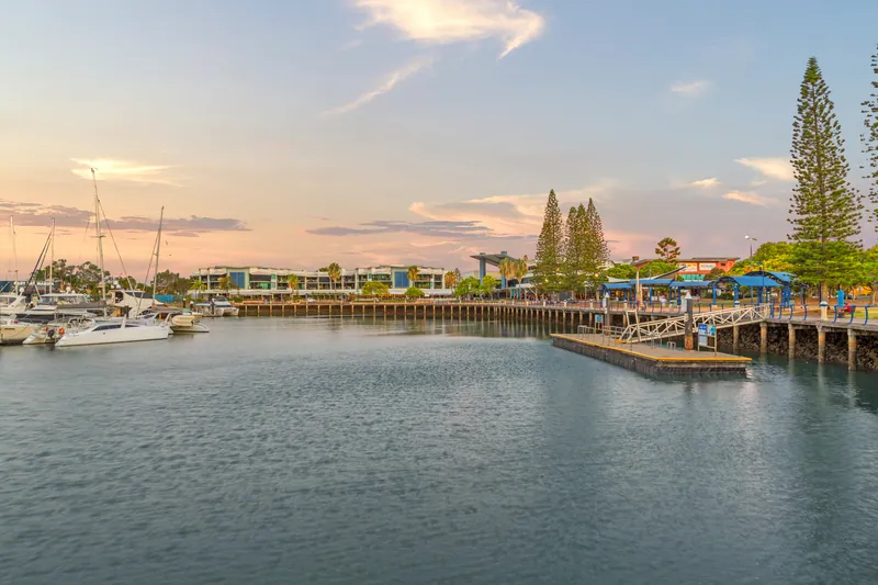 The Raby Bay Harbour boardwalk and marina at dusk, with an LJ Hooker sign on the building on the right